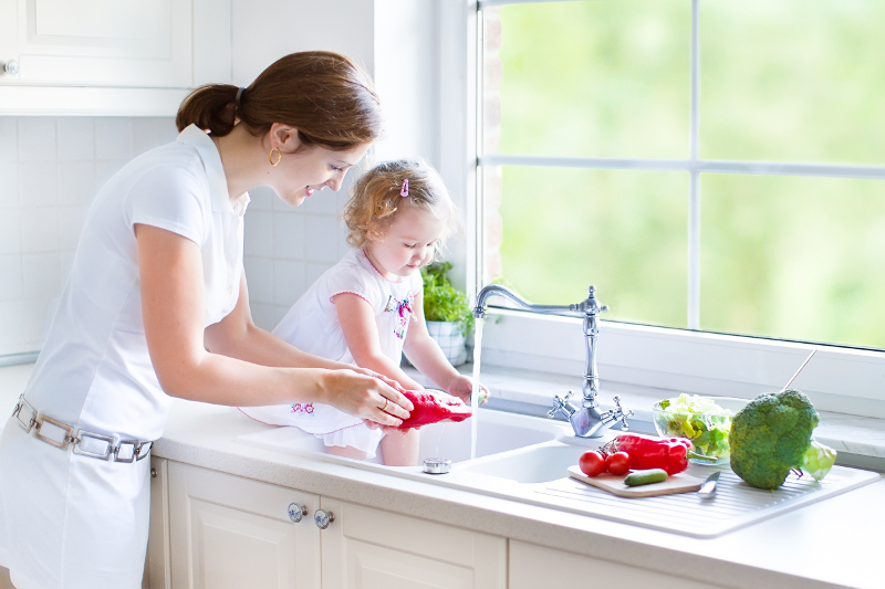 Matka z dzieckiem myjąca warzywa w umywalce