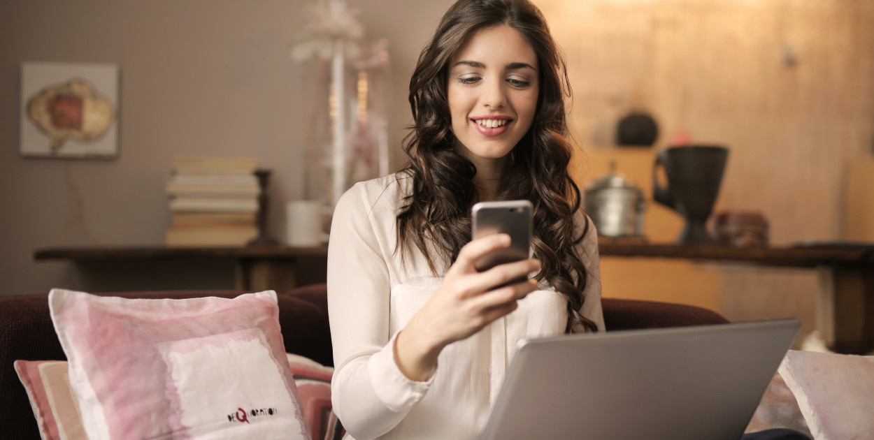 Zdjęcie dodane przez Andrea Piacquadio: https://www.pexels.com/pl-pl/zdjecie/kobieta-siedzi-na-kanapie-patrzac-na-telefon-z-laptopem-na-kolanach-920382/